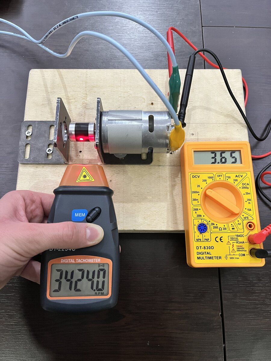 Measuring the back-EMF constant. A tachometer reads the shaft speed while a multimeter reads the terminal voltage; repeating this at several voltages gives the voltage-speed fit.